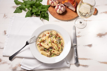 Penne pasta with carbonara sauce in white plate on wooden white background, soft light, angle view. Italian food