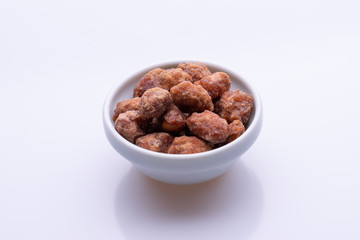 Peanuts praline sweet in a white bowl, on white background, soft light, copy space