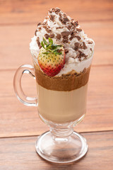 Cold coffee drink frappe (frappuccino), with whipped cream and chocolate nibs, with grains of coffee on wooden background