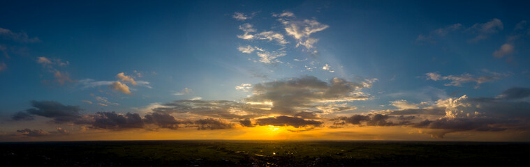 Fototapeta premium Panorama Top view Aerial photo from flying drone over village in Thailand.Cumulus sunset clouds with sun setting down on dark background.