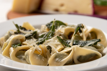Homemade tortellini with butter and sage in a white plate on white wooden table background. Soft light