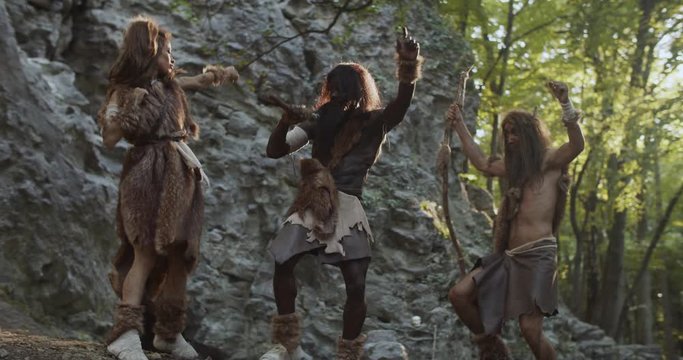 Happy tribe of cavemen neanderthals wearing animal skin holding weapon dancing having fun in prehistoric forest ancient bushman aboriginal evolution stone primitive cave slow motion
