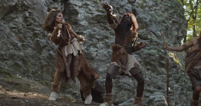 Funny tribe of cavemen neanderthals wearing animal skin holding weapon dancing having fun in prehistoric forest ancient bushman aboriginal evolution stone primitive cave slow motion