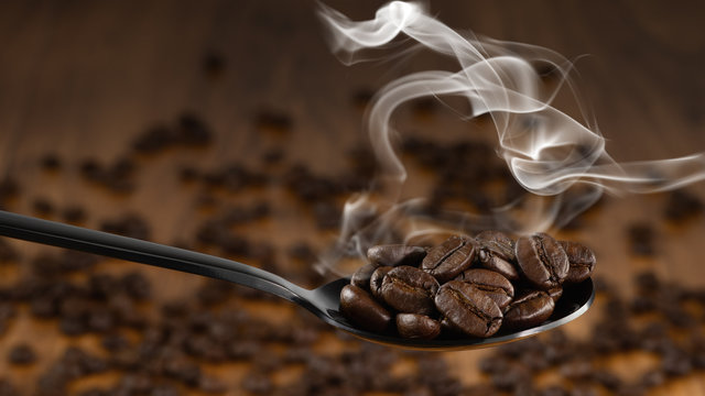 beverage background of roasted coffee beans in spoon with background of blurred background of coffee beans on wooden table