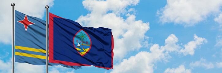 Aruba and Guam flag waving in the wind against white cloudy blue sky together. Diplomacy concept, international relations.