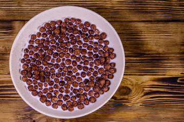 Ceramic plate with chocolate cereal balls in milk on wooden table. Top view