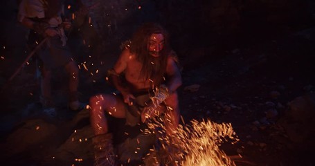 Near fire neanderthals wearing animal skin use tablet computer sitting in a cave stone fun male ancient history portrait evolution nature homo sapiens primitive campfire slow motion