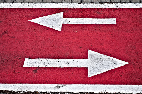 Left and right white dirrection arrows on neon red surface of a city biking lane.