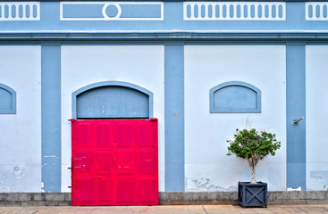 Red meteal sliding doors to a blue hangar and a potted green plant.