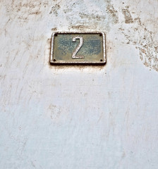 Old plate number 2, two, on a very weathered dusty wall surface, offset.