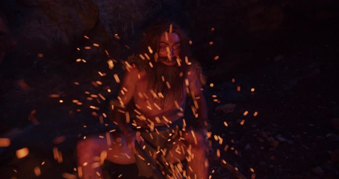 Portrait neanderthal man wearing animal skin holding weapon sitting by the fire in a cave stone fun male ancient history portrait evolution nature homo sapiens primitive campfire slow motion