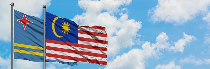 Aruba and Malaysia flag waving in the wind against white cloudy blue sky together. Diplomacy concept, international relations.