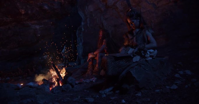 Surprised tride cavemen neanderthals wearing animal skin use tablet computer sitting by the fire in a cave stone fun male ancient history evolution nature homo sapiens primitive campfire slow motion