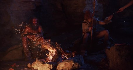 Cavemen neanderthals wearing animal skin play with fire use tablet computer sitting by the fire in a cave stone fun male ancient evolution homo sapiens primitive campfire slow motion