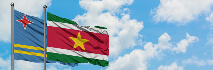 Obraz premium Aruba and Suriname flag waving in the wind against white cloudy blue sky together. Diplomacy concept, international relations.