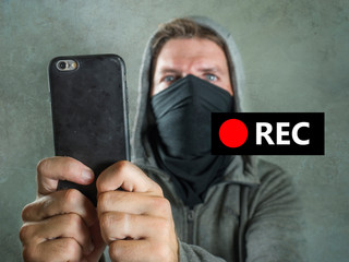 conceptual portrait of young rioter filming street chaos . ultra and radical man masked recording...
