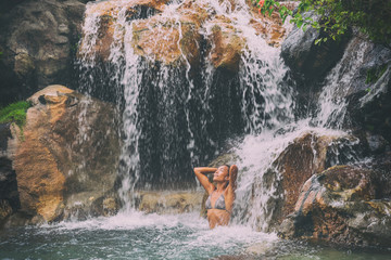 Waterfall woman relaxing in wellness nature water in tropical travel vacation background. Sexy bikini body care girl swimming in natural pool. Health and spa concept.
