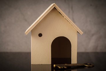 Home owning concept. Wooden house and key on a black background