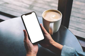 Mockup image of a woman holding black mobile phone with blank screen with coffee cup on the table