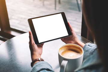 Mockup image of a woman holding black tablet with white blank desktop screen while drinking coffee