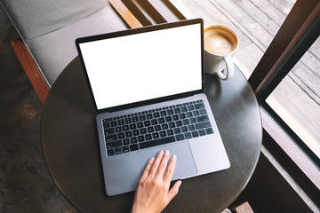 Top view mockup image of a hand using and touching on laptop touchpad with blank white desktop screen with coffee cup on the table