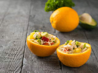 Avocado, chicken and bell pepper salad in two orange halves on a wooden table.