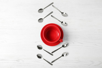 Fototapeta na wymiar Flat lay composition with teaspoons and red cup on white wooden table
