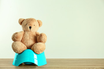 Teddy bear with blue potty on wooden table against light background, space for text. Toilet training