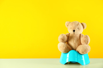 Teddy bear with blue potty on table against yellow background, space for text. Toilet training