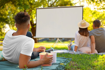 Young man with popcorn watching movie in open air cinema. Space for text