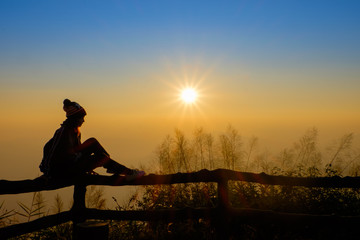 Woman tourist is a feeling relax, she is watching sunrise with mist in the morning, orange sky, viewpoint at Phu Ruea National Park, Loei, Thailand.