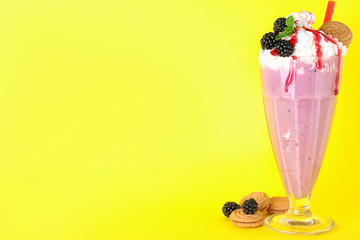 Tasty milk shake in glass, blackberries and cookies on yellow background. Space for text