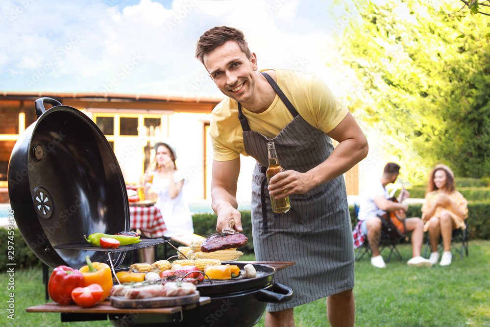 Wall mural young man with beer cooking on barbecue grill outdoors