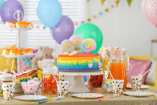 Bright birthday cake and other treats on table in decorated room
