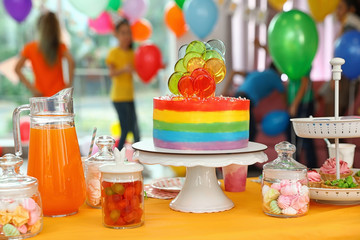 Bright birthday cake and other treats on table in decorated room