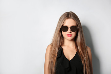 Young woman wearing stylish sunglasses on light background. Space for text