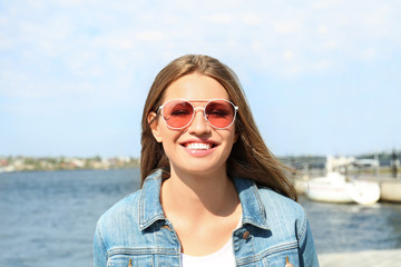 Young woman wearing stylish sunglasses near river