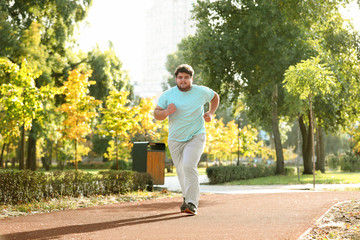 Young overweight man running in park on sunny day - obrazy, fototapety, plakaty