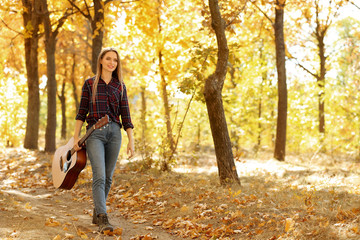 Teen girl with acoustic guitar in autumn park