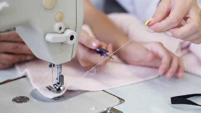 The color of fabric is pink. The sewing machine is white. Women makes clothes with little girl.