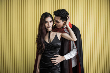 Asian young couple in costume witch and dracula on yellow background.