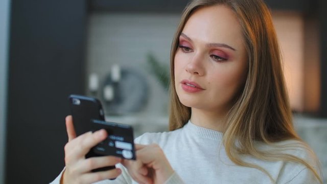 A young beautiful woman holds a smartphone and a credit card while paying for purchases and entering a pincode to pay for delivery. Online shopping