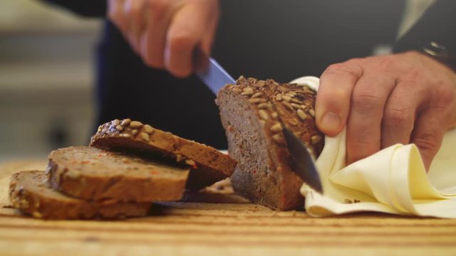 4K Slow motion close up of a a fresh whole-grain bread being sliced with a knife. Grains falling of the loaf with slight camera movement and a filmed with a wide aperture