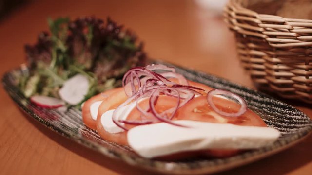 4K close up of a food plate with sliced cheese, tomatos, onions and salat and a bread basket with a focus pull. Shot with a wide aperture.