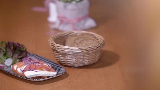 4K Camera pan of a food plate with sliced cheese, tomatos, onions and salat and a bread basket standing on a table. Object reveal from blurred background. Shot with a wide aperture.