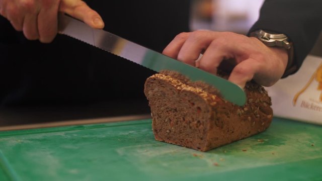 4K Slow motion shot of a a fresh whole-grain bread being sliced with a knife. Grains falling of the loaf with slight camera movement and a filmed with a wide aperture
