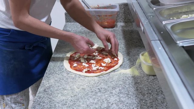 Pizza Maker hands putting mozzarella on pepperoni pizza, Medium Shot