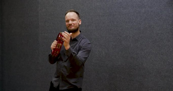 Smiling Caucasian musician playing tambourine looking at the camera, with high quality sound