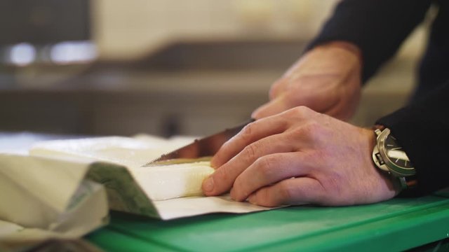4K Slow motion close up of a fresh cheese being sliced with a knife. Filmed with a wide aperture