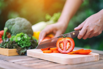 Closeup image of a woman cutting and chopping tomato by knife on wooden board - Powered by Adobe